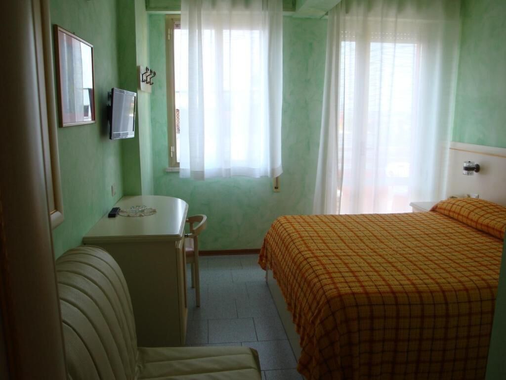 Ein Zimmer mit einem Bett, einem Schreibtisch, einem Stuhl und einem fenster mit Vorhängen.