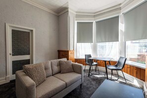 A living room with a sofa, two chairs, a small table, and large windows with blinds. - St Andrews by Guestz (Lytham St Annes)