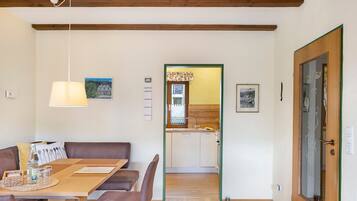 Ein Essbereich mit Holztisch und -stühlen, einer Hängeleuchte und Blick in eine Küche mit Holzschränken und einem Fenster.