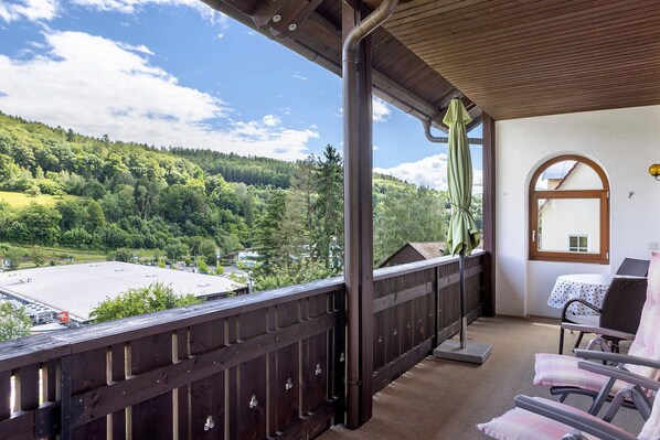 Un balcon donnant sur un paysage verdoyant, une table avec une chaise, et une fenêtre à l’encadrement en arc de cercle.