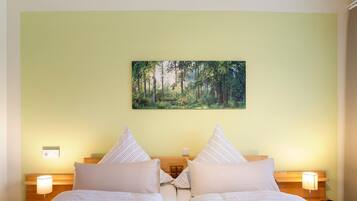 Un letto matrimoniale con cuscini a righe, un comodino con una lampada e un quadro raffigurante una foresta al muro.