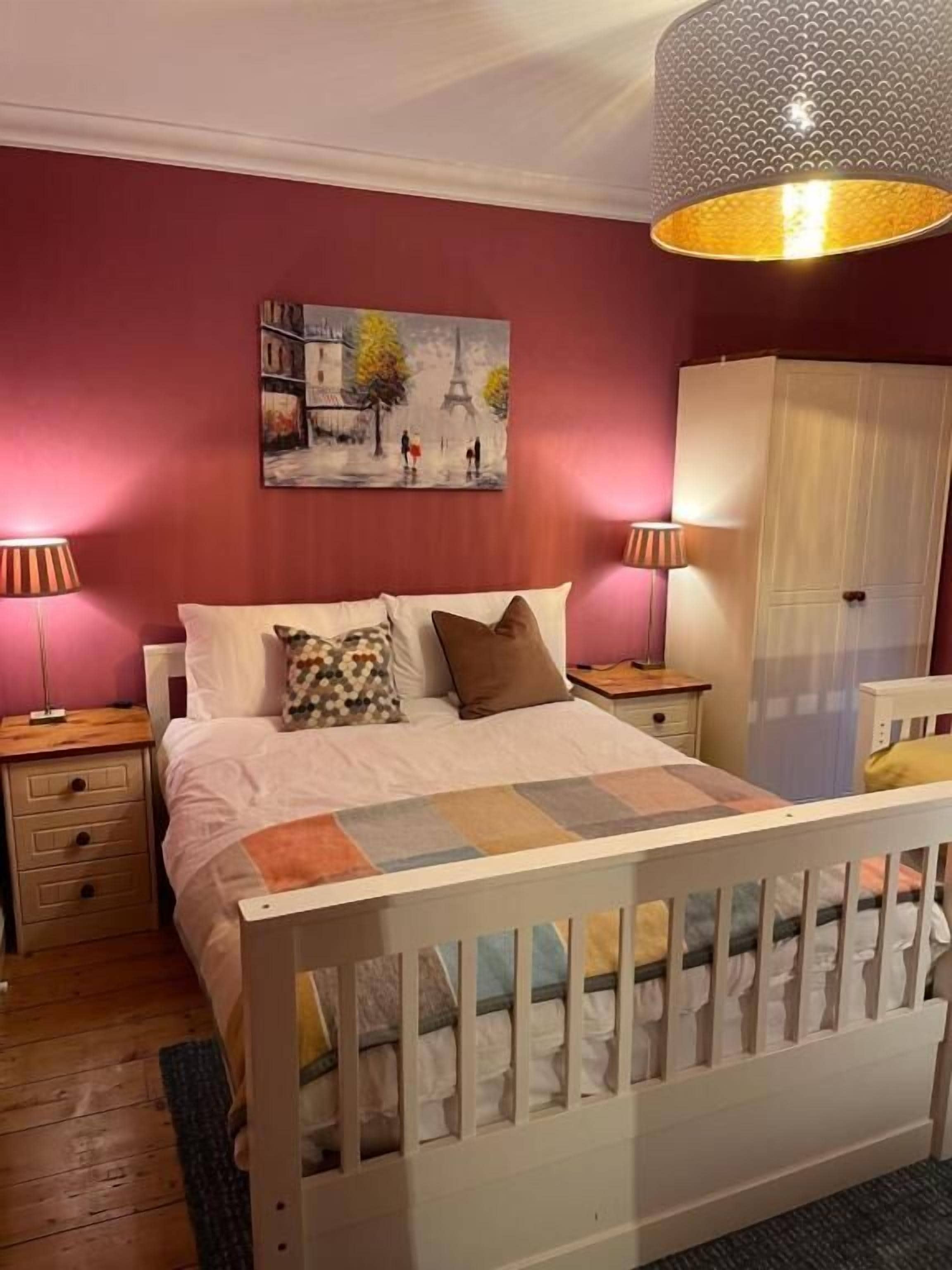 Un dormitorio con cama, mesita de noche, cómoda, armario y un cuadro de la Torre Eiffel.