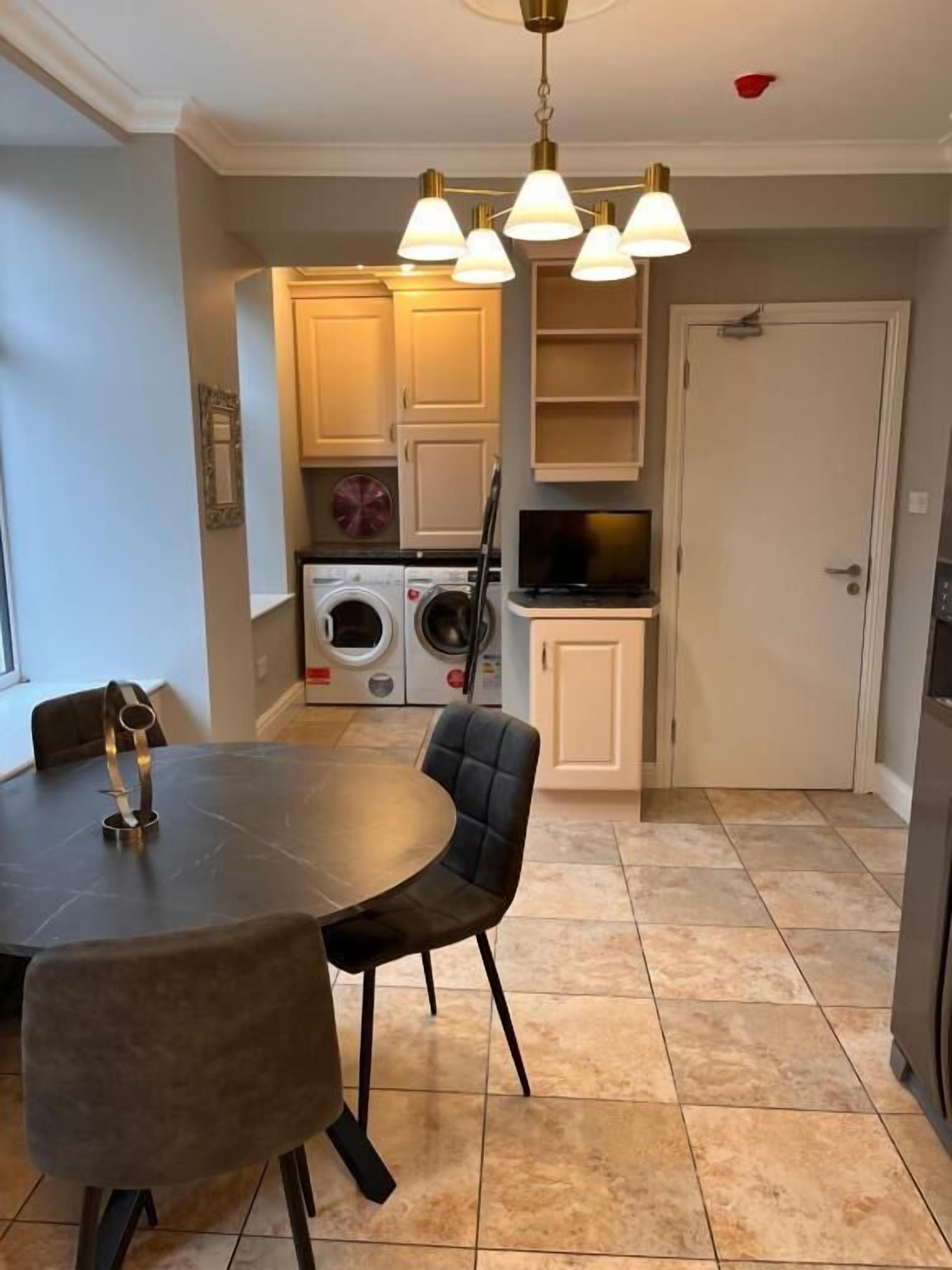 A dining area with a table and chairs, a washing machine, a television, and a door in a residential setting.