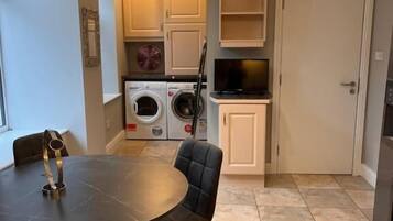 A dining area with a table and chairs, a washing machine, a television, and a door in a residential setting.