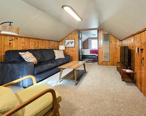 Una habitación acogedora con un sofá, una mesita de madera, un televisor y una puerta que da a otra habitación.