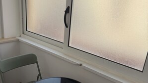 Una habitación con una mesa redonda y dos sillas, una ventana con vidrio esmerilado y una pared blanca.