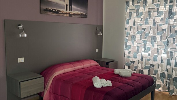 Un dormitorio con cama, mesitas de noche, un cuadro en la pared y una cortina estampada.
