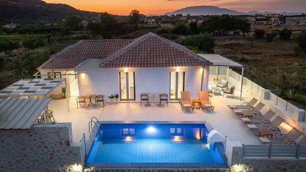 Eine Villa mit Pool, Außenbereich und Blick auf die Landschaft bei Sonnenuntergang.