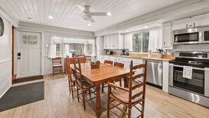 Una cocina moderna con comedor, sillas de madera, una mesa grande, electrodomésticos de acero inoxidable y un ventilador de techo.