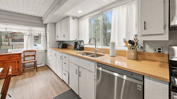 Una cocina con lavavajillas, cafetera y ventana con cortinas.