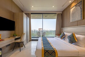 A hotel room with a bed, a desk, a chair, a TV, and a balcony with a view. - Aurea Avasa (Gurugram)