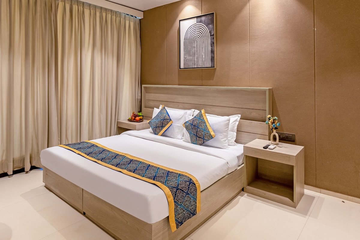 A modern hotel room with a large bed, a bedside table, a nightstand, a ceiling fan, and a wall-mounted artwork.