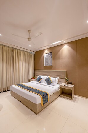 A modern hotel room with a large bed, a bedside table, a nightstand, a ceiling fan, and a wall-mounted artwork. - Aurea Avasa (Gurugram)