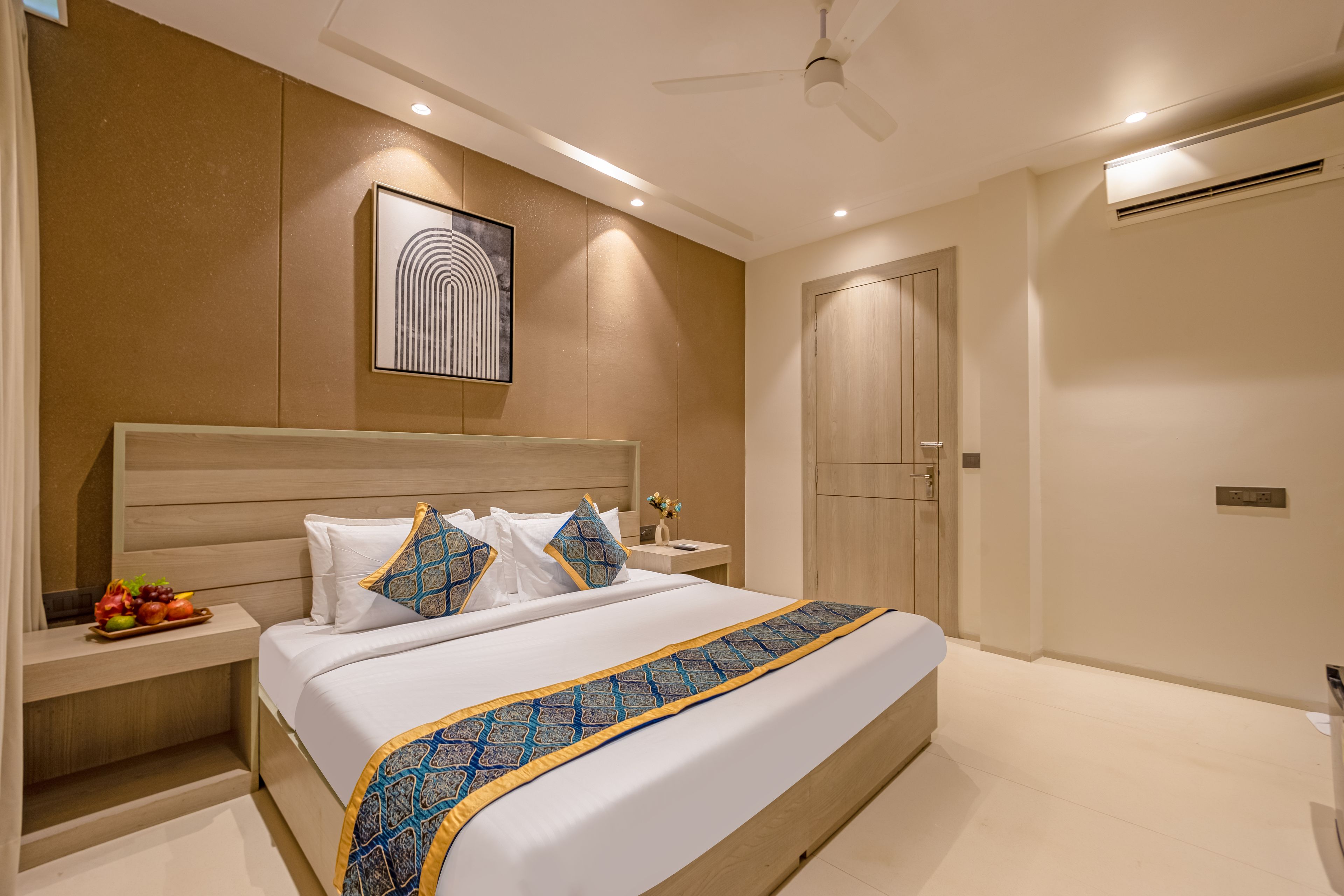 Una habitación de hotel con una cama grande, mesitas de noche, un tocador, un ventilador de techo y una puerta.