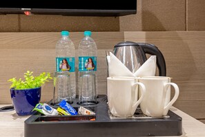 Un área de cocina americana con cafetera, dos tazas, una botella de agua, una planta y algunos alimentos.