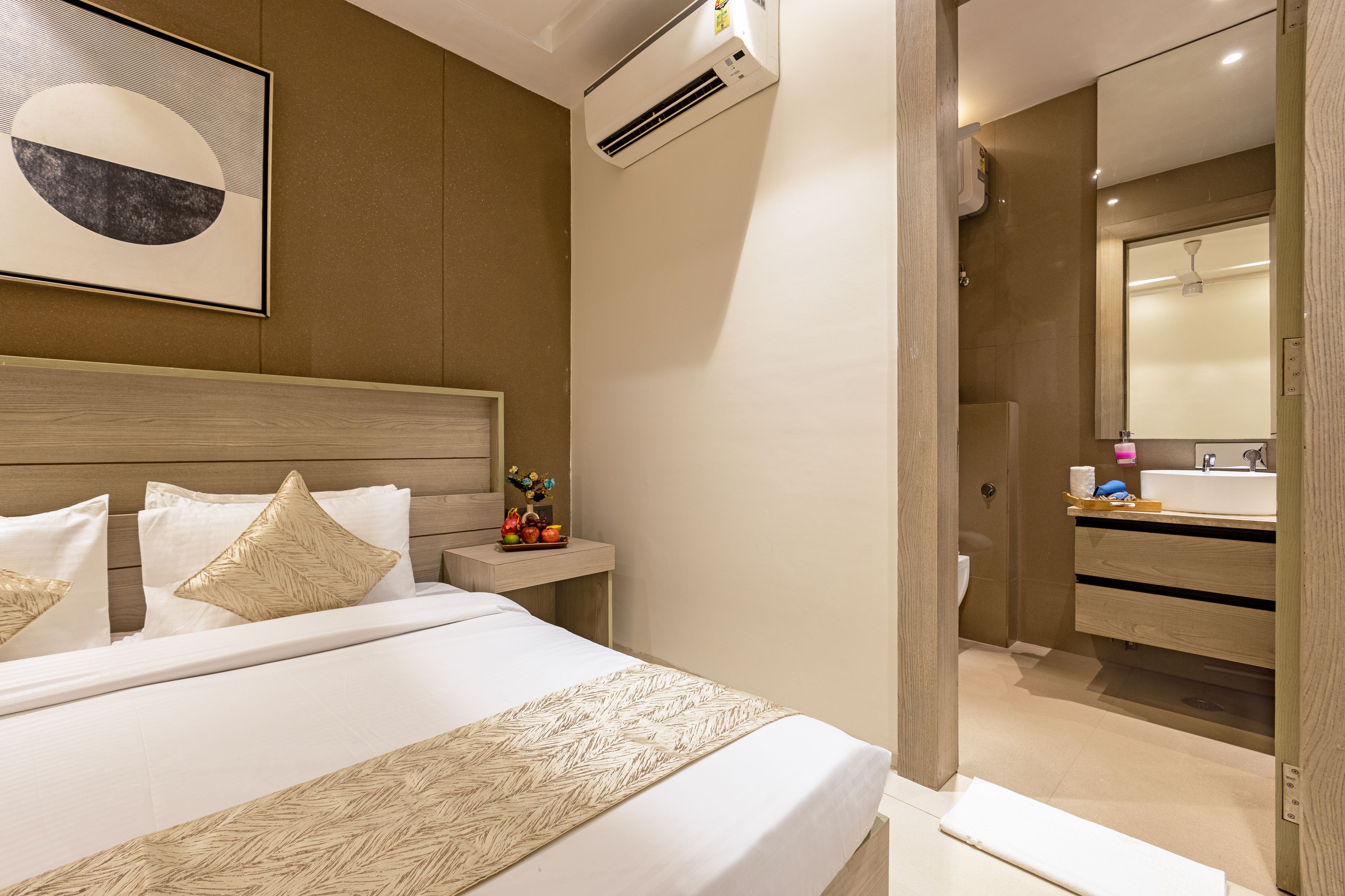 Habitación de hotel con cama, mesita de noche y baño con lavamanos y espejo.