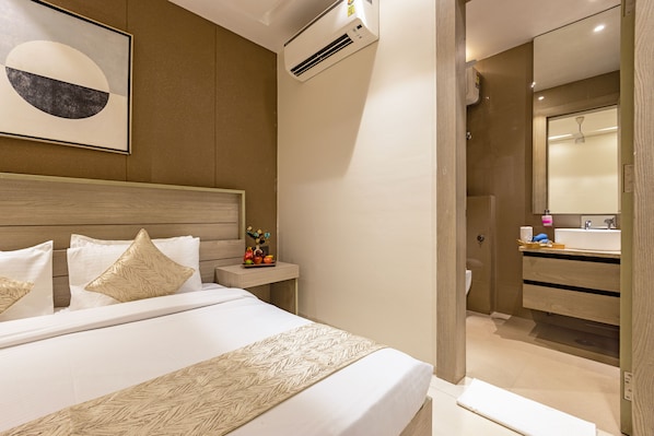 A hotel room with a bed, bedside table, and a bathroom with a sink and mirror. - Aurea Avasa (Gurugram)