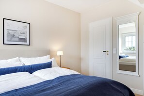 A hotel room with a bed, a nightstand, a lamp, a door, and a framed picture on the wall. - Inselhüs on Sylt: family-friendly, 150 m², wood-burning stove & wellness facilities (Wenningstedt-Braderup (Sylt))