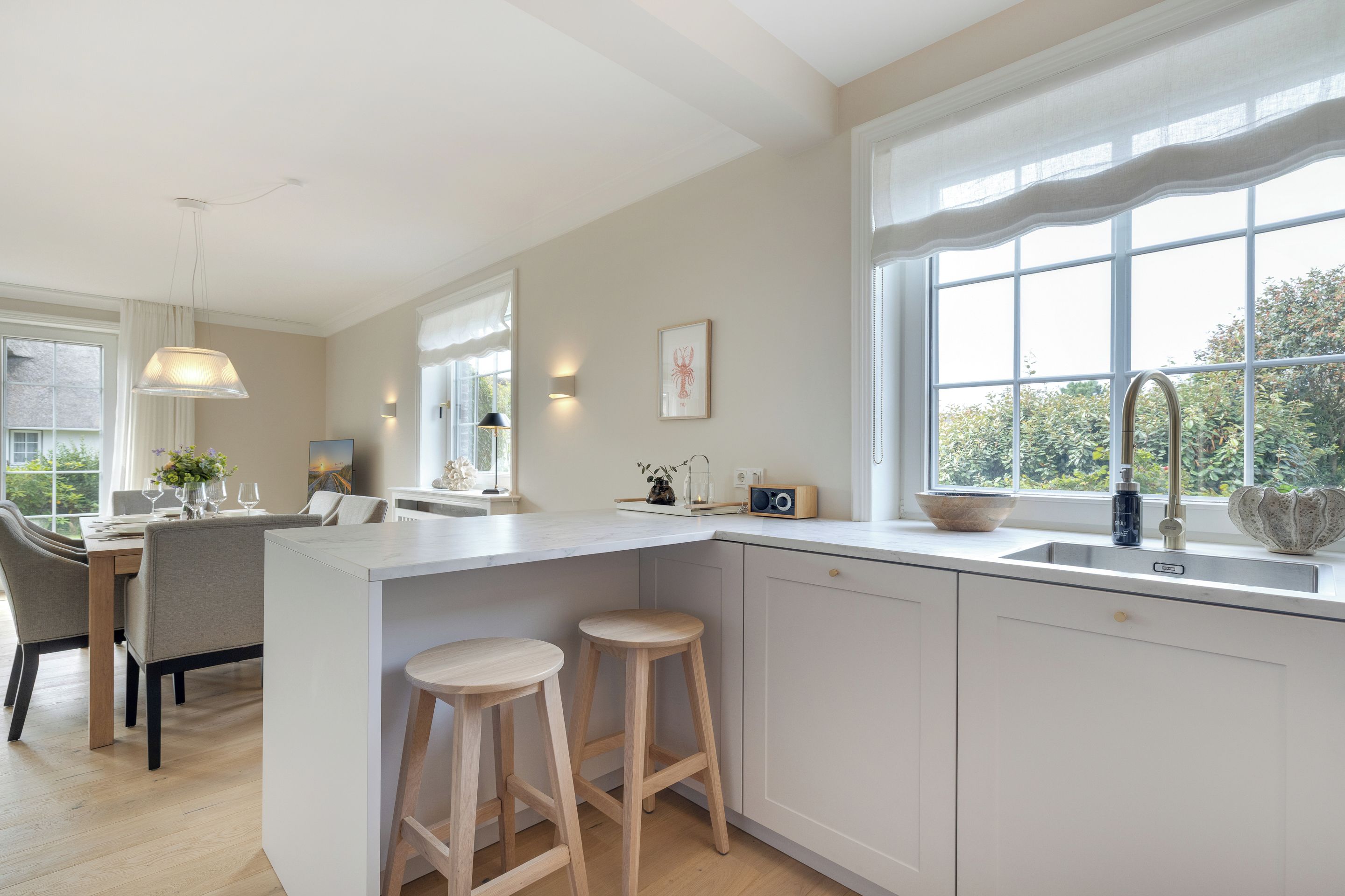 A modern kitchen with a large island, bar stools, and a view of greenery outside.