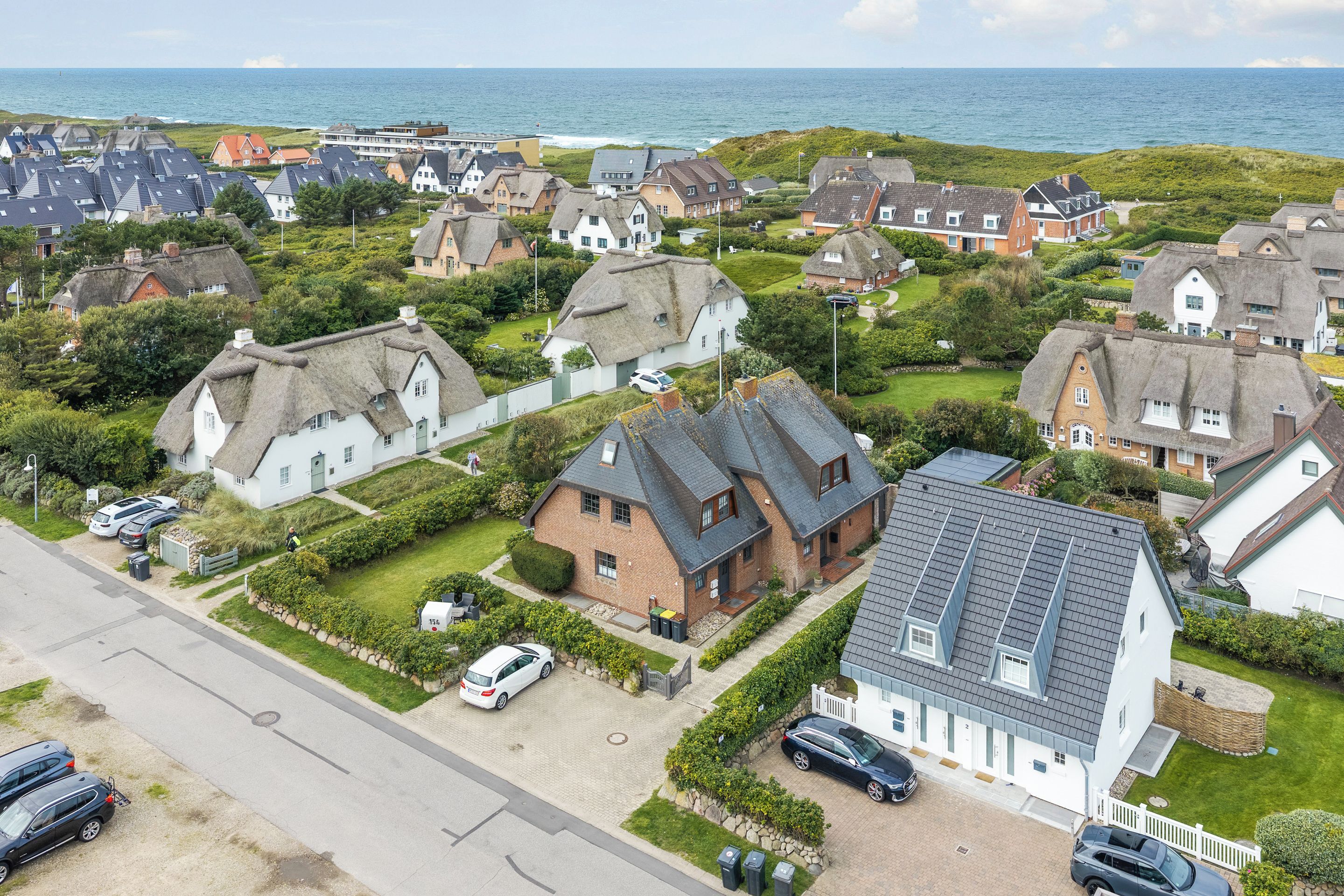 Een woonwijk met huizen, waarvan enkele rieten daken hebben, en uitzicht op de zee.