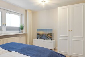 Un dormitorio con cama, ventana, televisor sobre un mueble bajo y armario.
