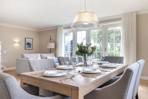 A dining area with a wooden table set for six, surrounded by grey upholstered chairs. - Inselhüs on Sylt: family-friendly, 150 m², wood-burning stove & wellness facilities (Wenningstedt-Braderup (Sylt))