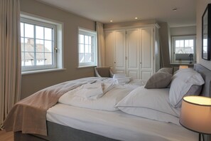 Ein Schlafzimmer mit einem Bett, zwei Fenstern, einem Kleiderschrank und einer Nachttischlampe.