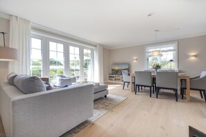 A modern living room with a sofa, dining table, and chairs. There is a TV and a bookshelf in the background. - Inselhüs on Sylt: family-friendly, 150 m², wood-burning stove & wellness facilities (Wenningstedt-Braderup (Sylt))