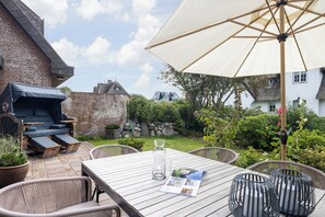 An outdoor patio with a wooden table, chairs, a grill, and a large umbrella. - Inselhüs on Sylt: family-friendly, 150 m², wood-burning stove & wellness facilities (Wenningstedt-Braderup (Sylt))