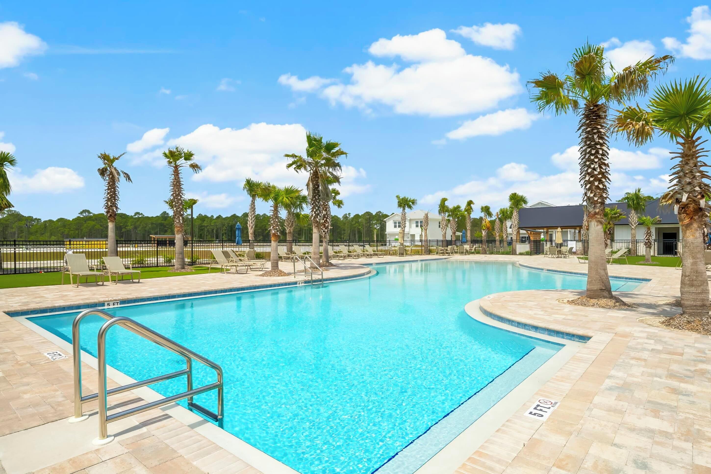 A swimming pool with a metal ladder, surrounded by palm trees and lounge chairs, with a clear blue sky.
