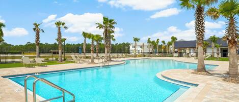 A swimming pool with a metal ladder, surrounded by palm trees and lounge chairs, with a clear blue sky.