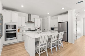 A modern kitchen with white cabinetry, stainless steel appliances, and a central island with seating. - Parkside on 30A by Panhandle Getaways (Santa Rosa Beach)