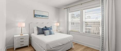 A bedroom with a bed, bedside tables, lamps, a window with blinds, and a painting on the wall.