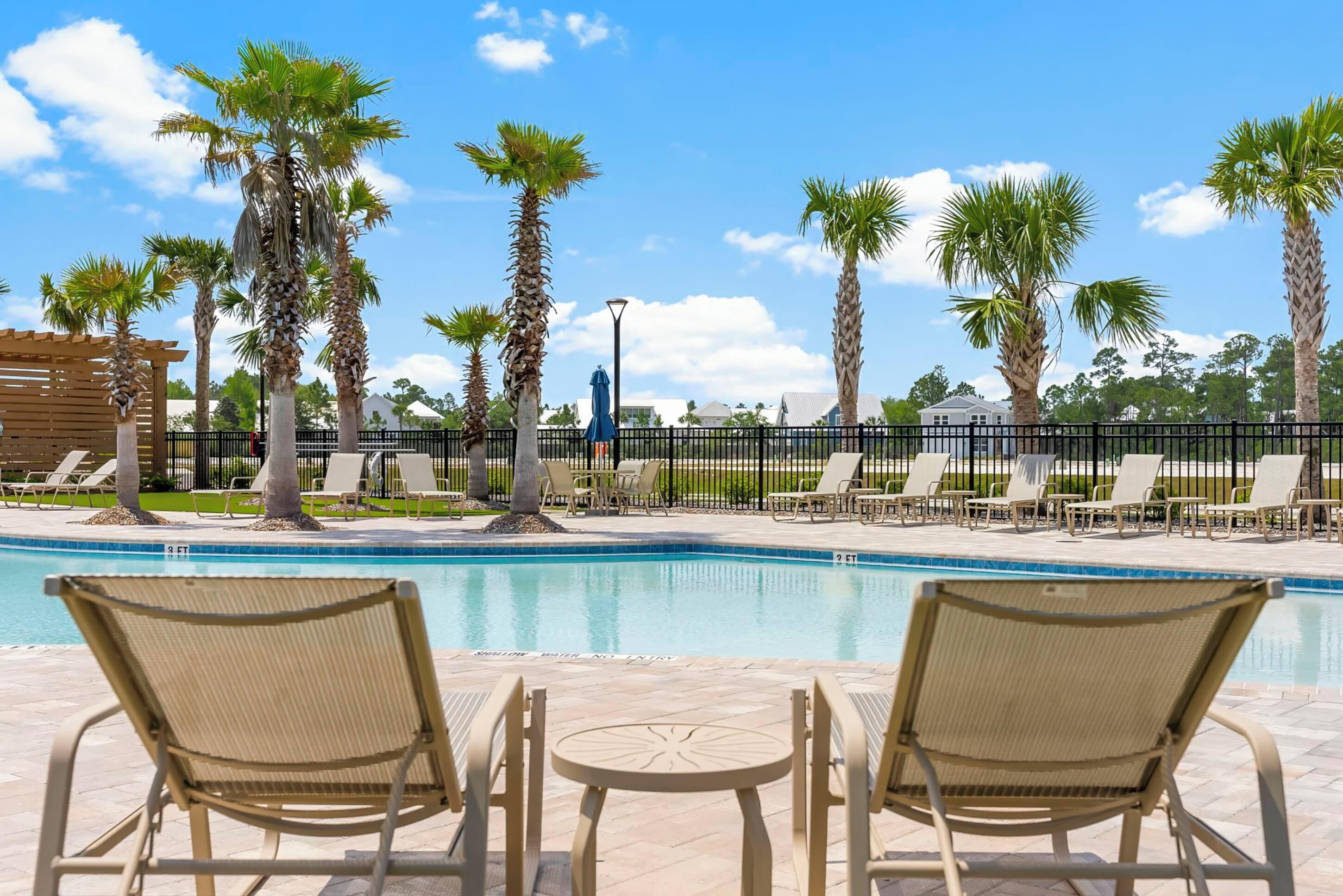A pool area with lounge chairs, palm trees, and a pergola.