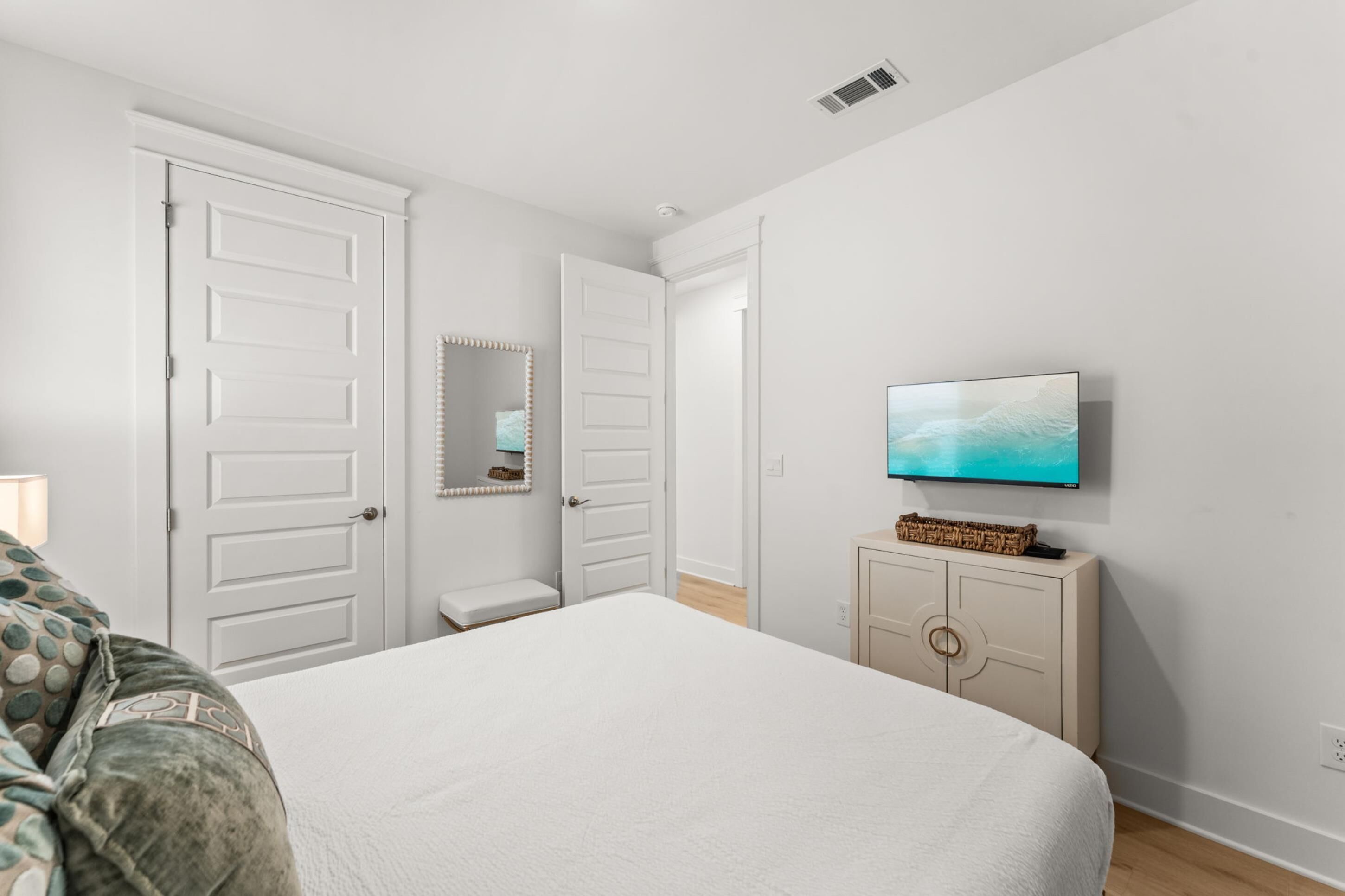 A bedroom with a bed, a television, a dresser, and a door leading to another room.
