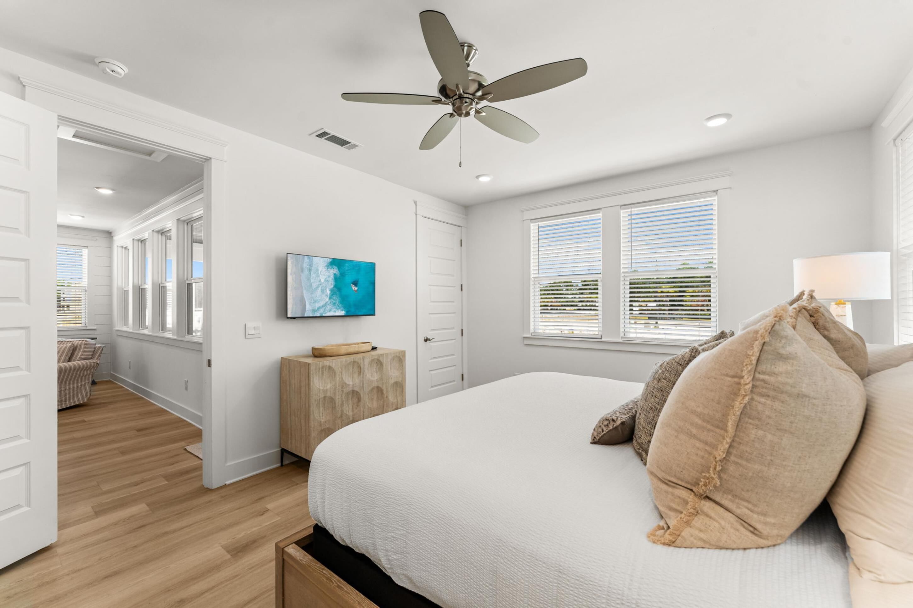 A bedroom with a bed, ceiling fan, artwork, and a window with blinds.