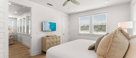 A bedroom with a bed, ceiling fan, artwork, and a window with blinds.
