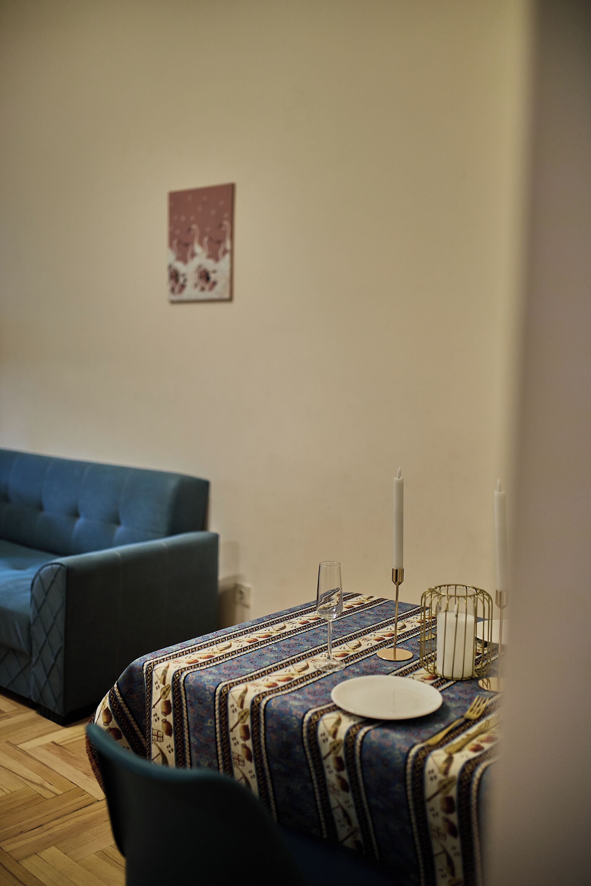 Quarto com sofá azul, mesa com toalha estampada, vela e copo.