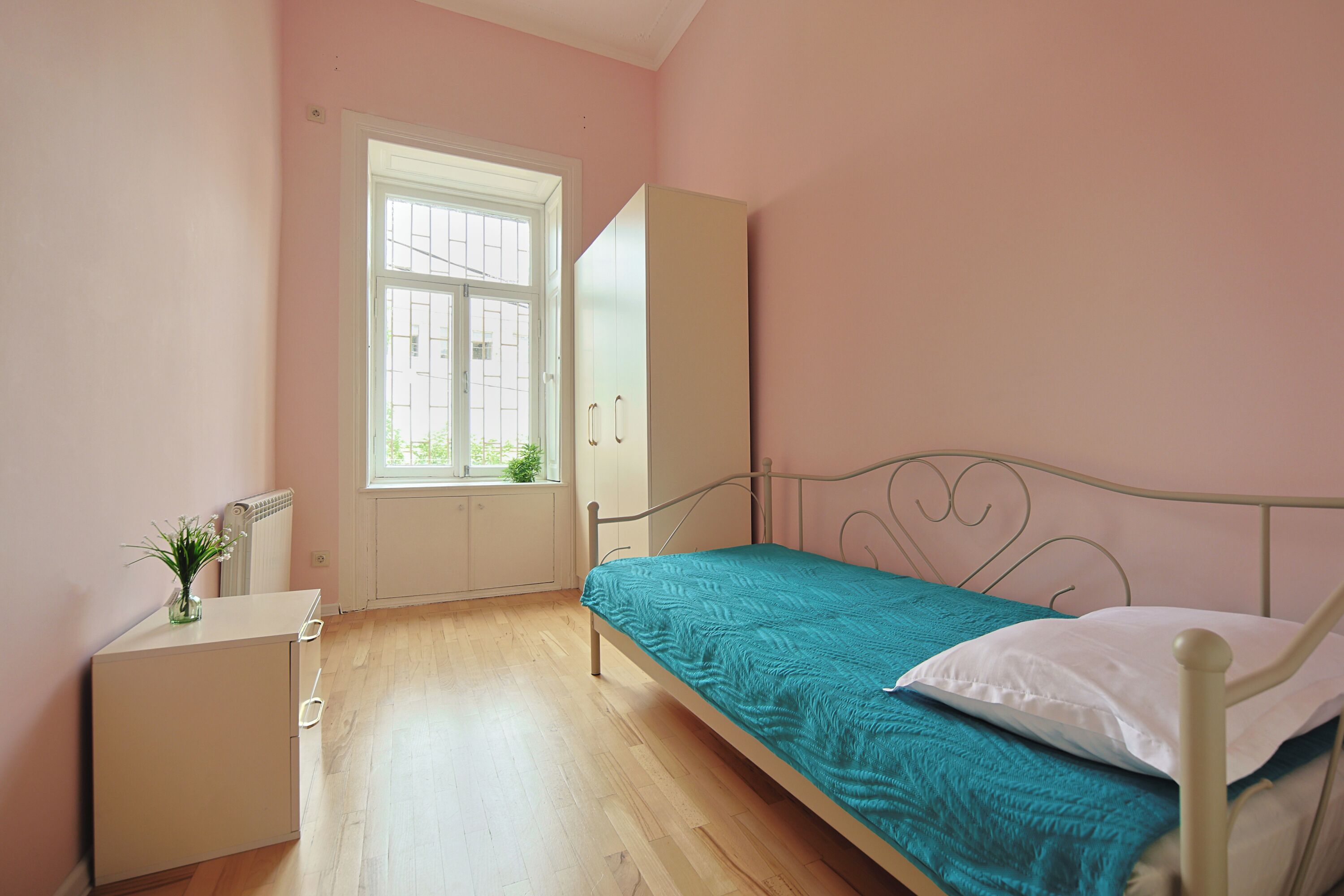 A bedroom with a bed, a wardrobe, a small table, and a window.