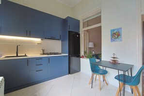 Une cuisine moderne avec des meubles bleus, un réfrigérateur noir et un coin repas comprenant deux chaises bleues et une table.