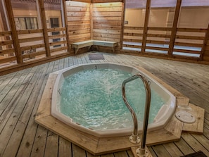 Una terraza de madera con un jacuzzi, bancos y un muro de madera.