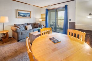 Una sala de estar acogedora con un sofá, una mesa de comedor de madera y vistas a través de un ventanal.