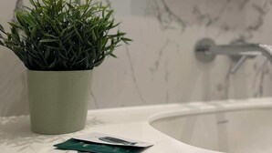 A bathroom with a marble wall, a white sink, and a potted plant. - Cute Studio Old Town (Poznań)