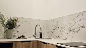 A modern kitchen with a marble backsplash, a built-in sink, and a wooden cabinet. - Cute Studio Old Town (Poznań)