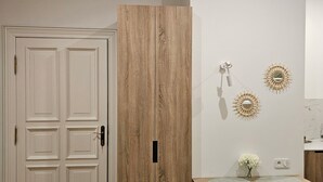 A room with a white door, a wooden wardrobe, a wall-mounted air conditioner, and decorative wall sconces. - Cute Studio Old Town (Poznań)