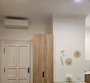 Ein Zimmer mit einer weißen Tür, einem Holzschrank, einer fest installierten Klimaanlage und dekorativen Wandleuchten.