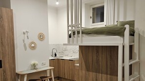 A compact room with a bunk bed, a small kitchenette, and a desk with a chair. - Cute Studio Old Town (Poznań)