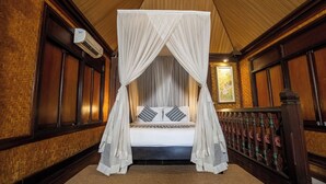 A room with a four-poster canopy bed, a wooden floor, and a wall-mounted air conditioning unit. - Alpin Resort and Villa Ubud (Ubud)