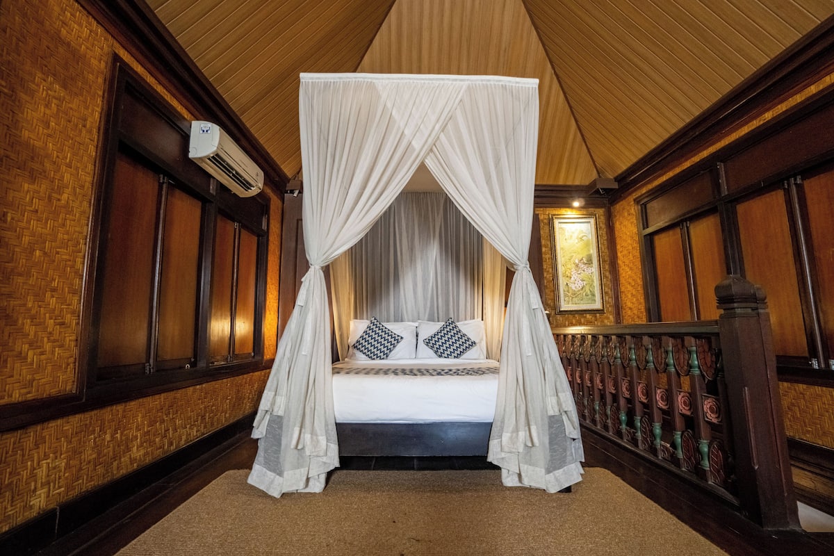 A room with a four-poster canopy bed, a wooden floor, and a wall-mounted air conditioning unit.