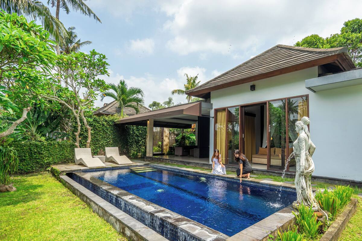 A swimming pool with lounge chairs, a statue, and a modern house with large windows.